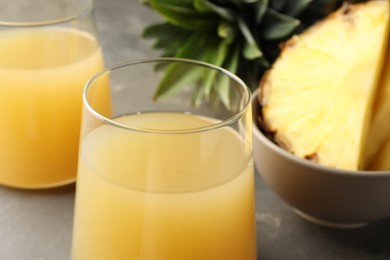 Photo of Tasty pineapple juice in glasses and fruits on grey table, closeup