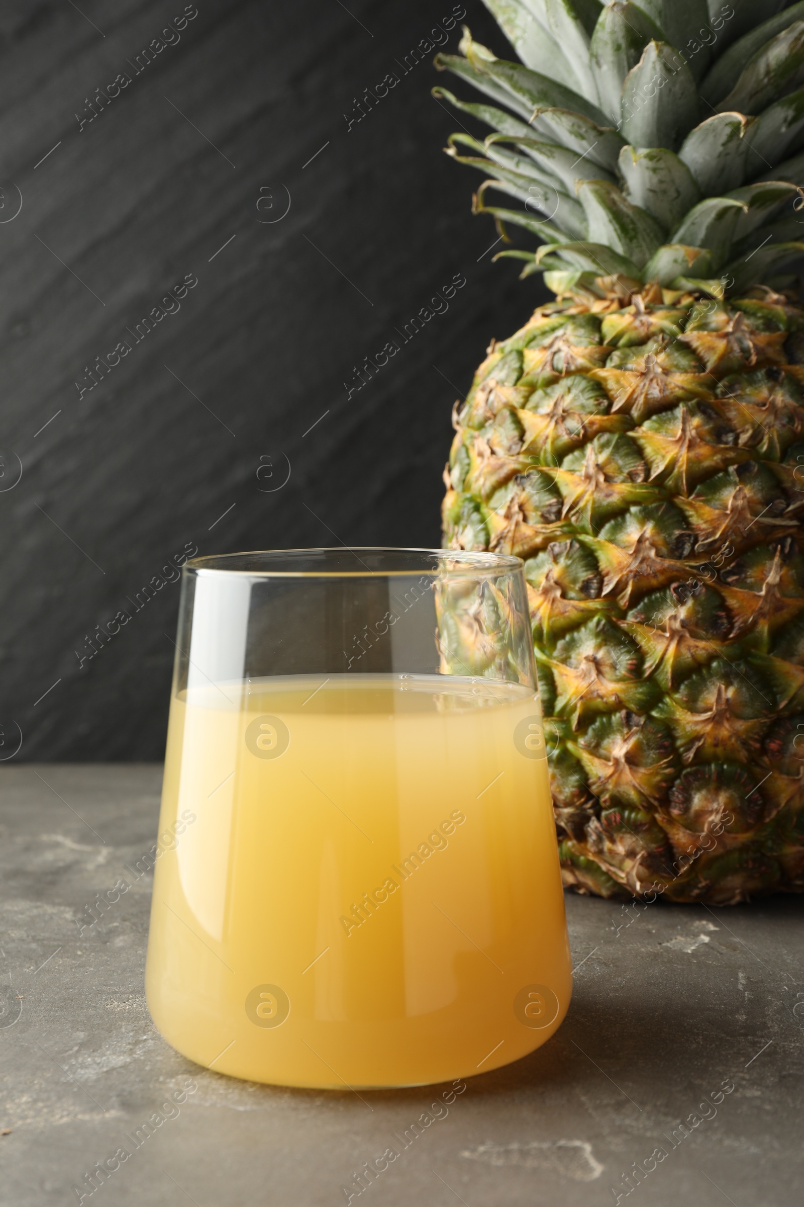 Photo of Tasty pineapple juice in glass and fruit on grey textured table