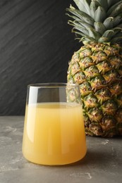 Photo of Tasty pineapple juice in glass and fruit on grey textured table