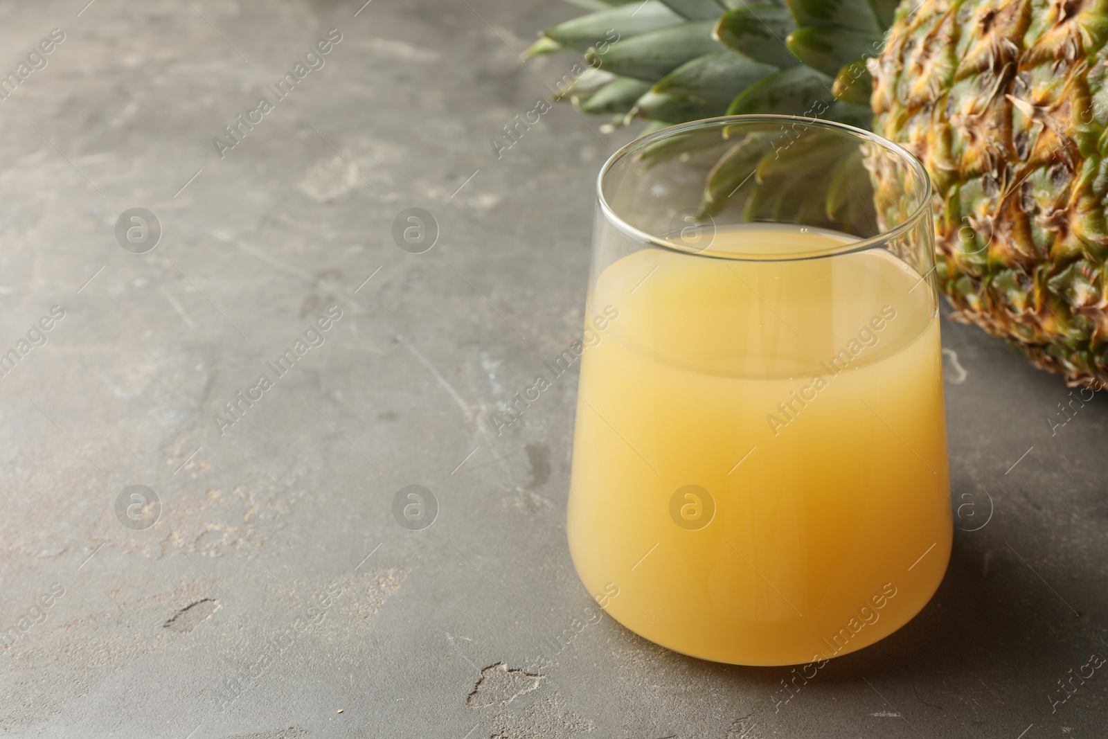 Photo of Tasty pineapple juice in glass and fruit on grey textured table, closeup. Space for text