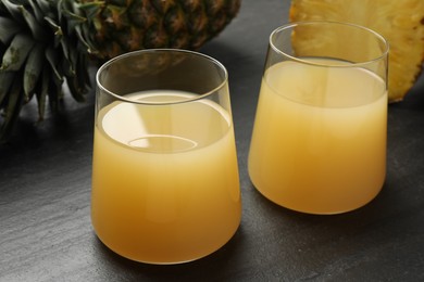 Photo of Tasty pineapple juice in glasses and fruits on grey textured table, closeup