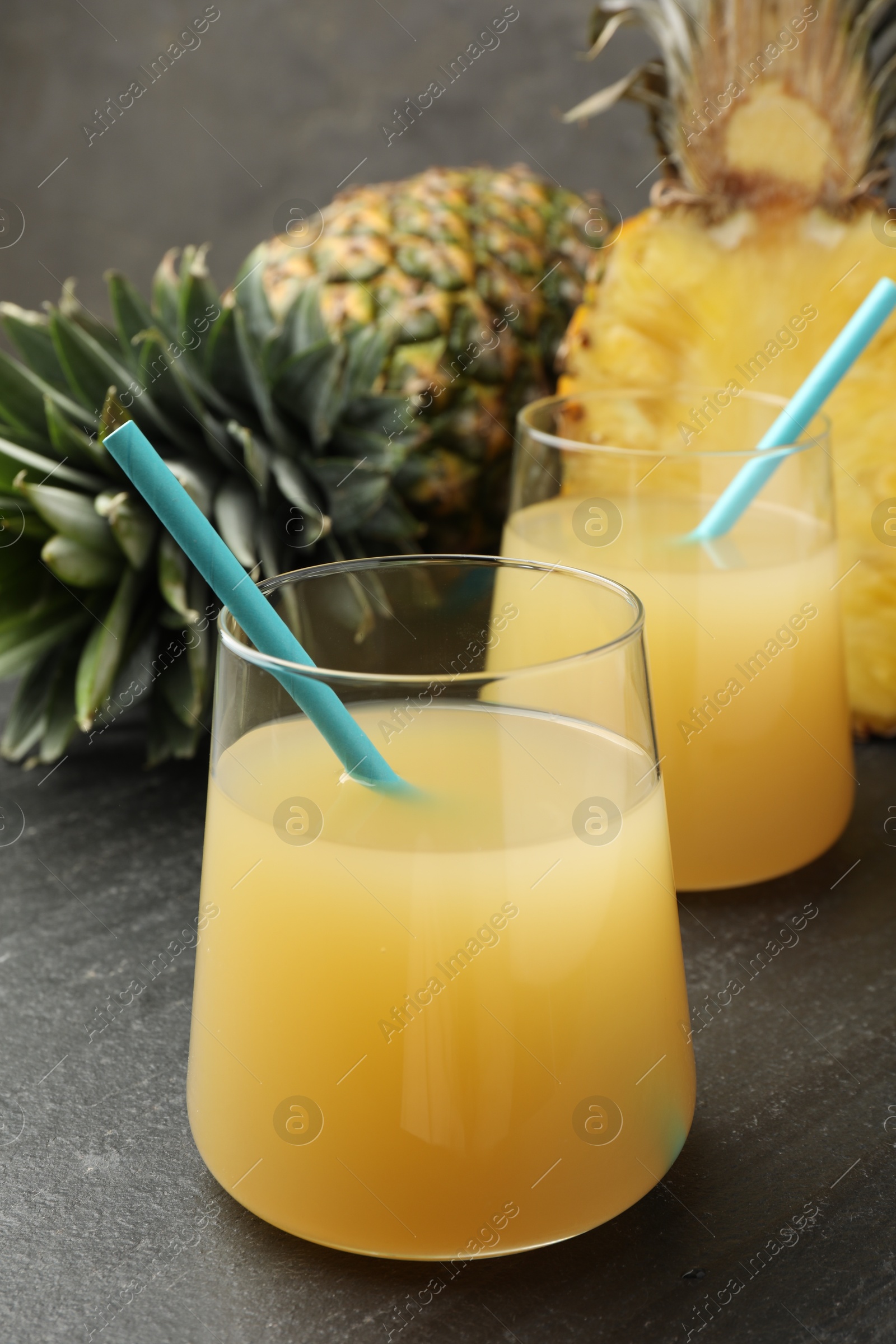 Photo of Tasty pineapple juice in glasses and fruits on grey textured table, closeup