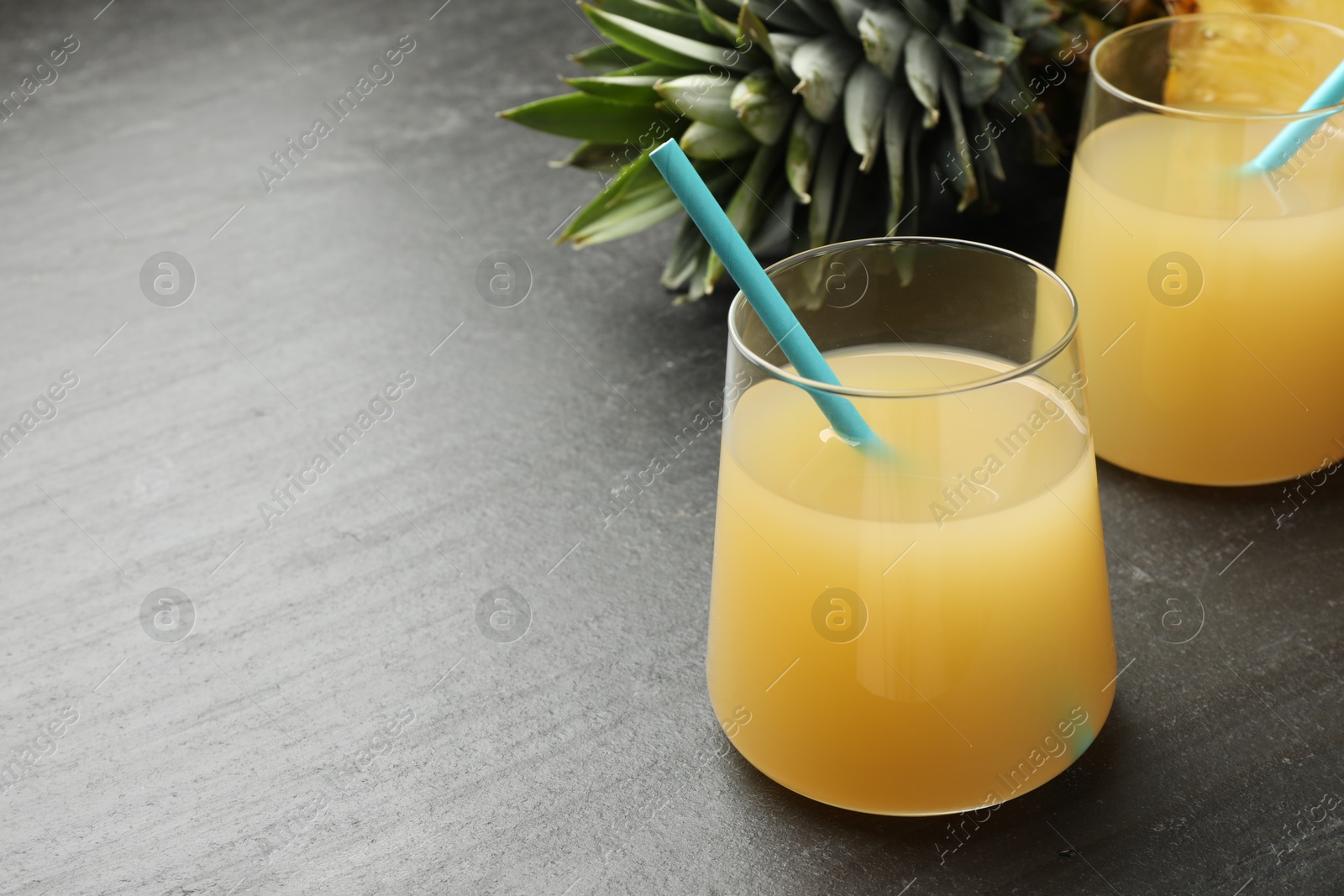 Photo of Tasty pineapple juice in glasses and fruit on grey textured table, closeup. Space for text