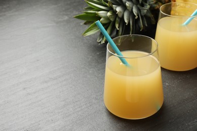 Photo of Tasty pineapple juice in glasses and fruit on grey textured table, closeup. Space for text