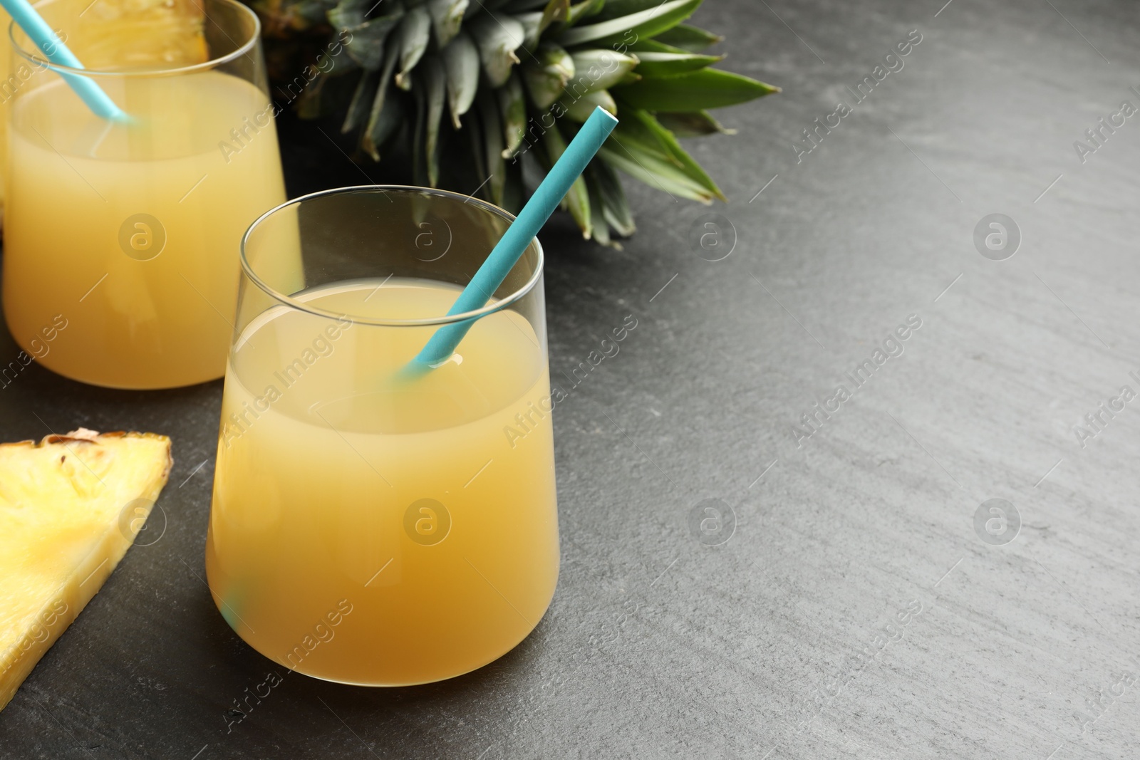 Photo of Tasty pineapple juice in glasses and fruit on grey textured table, closeup. Space for text