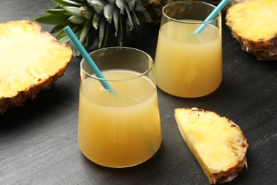 Photo of Tasty pineapple juice in glasses and fruits on grey textured table, closeup