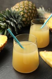 Photo of Tasty pineapple juice in glasses and fruits on grey textured table, closeup