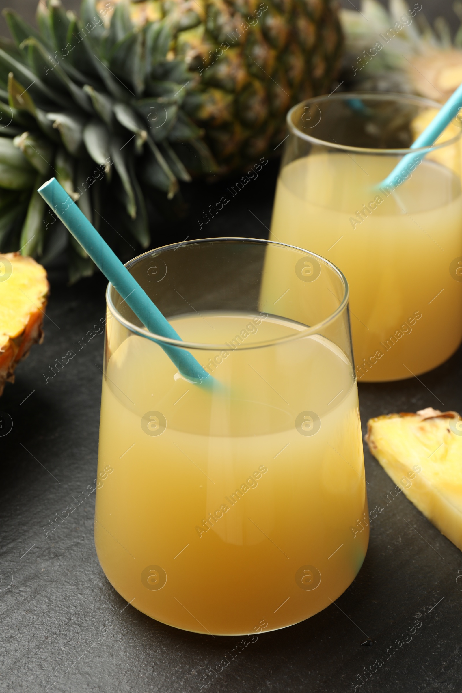 Photo of Tasty pineapple juice in glasses and fruits on grey textured table, closeup