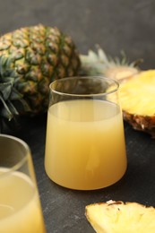 Photo of Tasty pineapple juice in glass and fruits on grey textured table, closeup