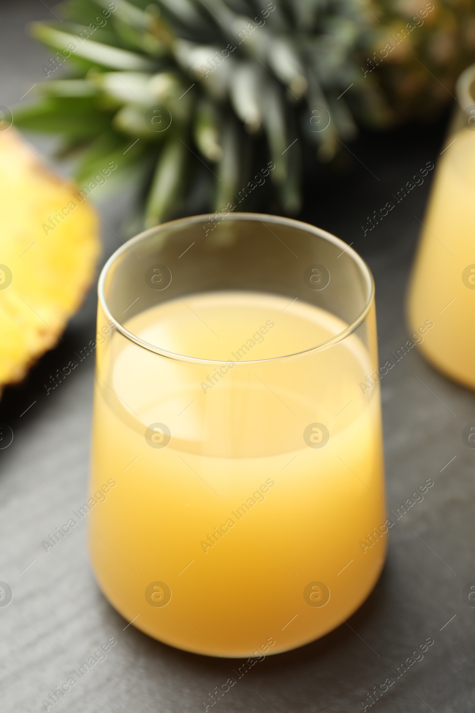 Photo of Tasty pineapple juice in glass and fruit on grey textured table, closeup