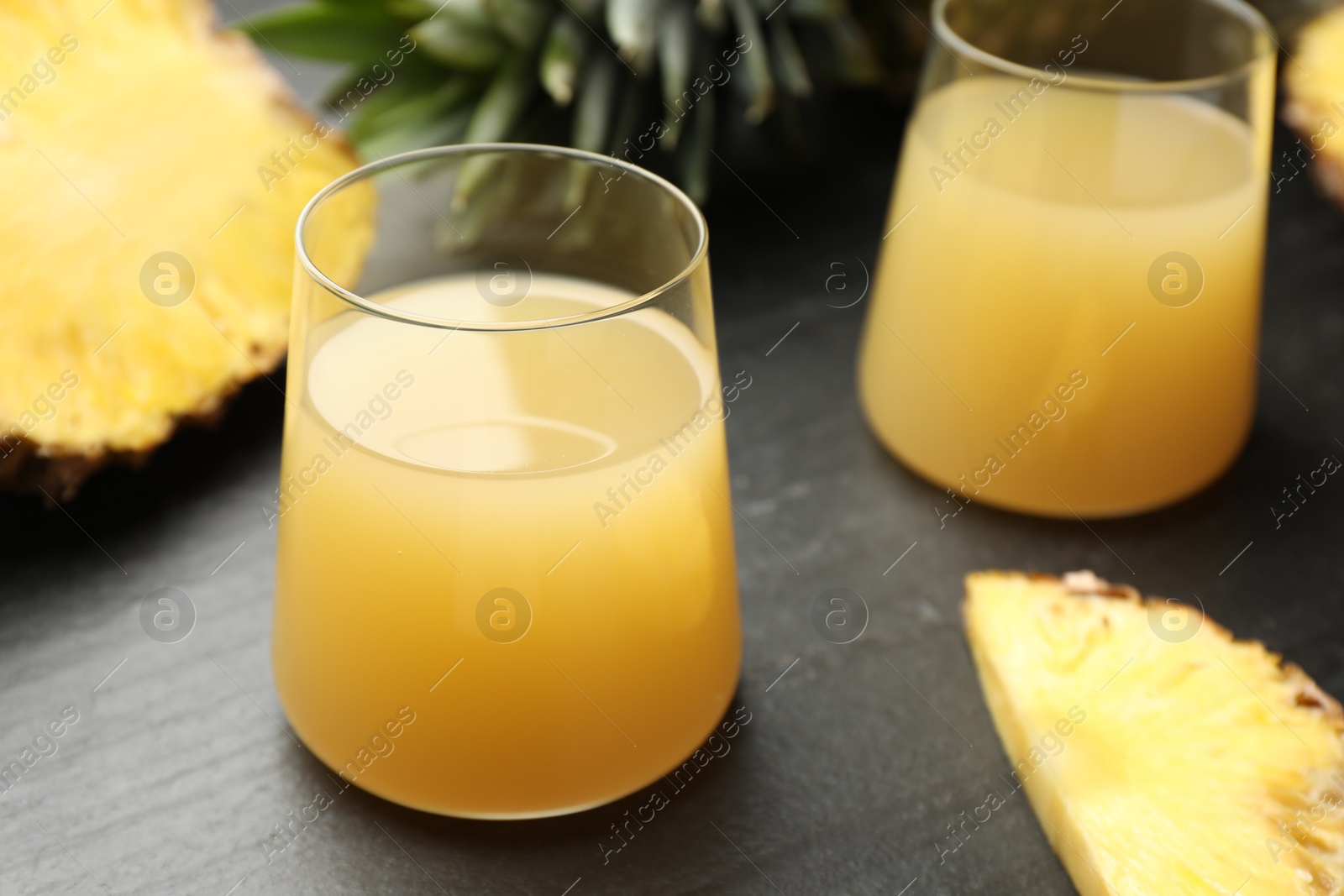 Photo of Tasty pineapple juice in glasses and fruit on grey textured table, closeup