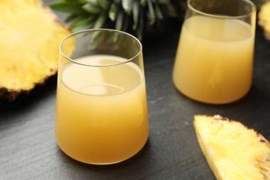 Photo of Tasty pineapple juice in glasses and fruit on grey textured table, closeup