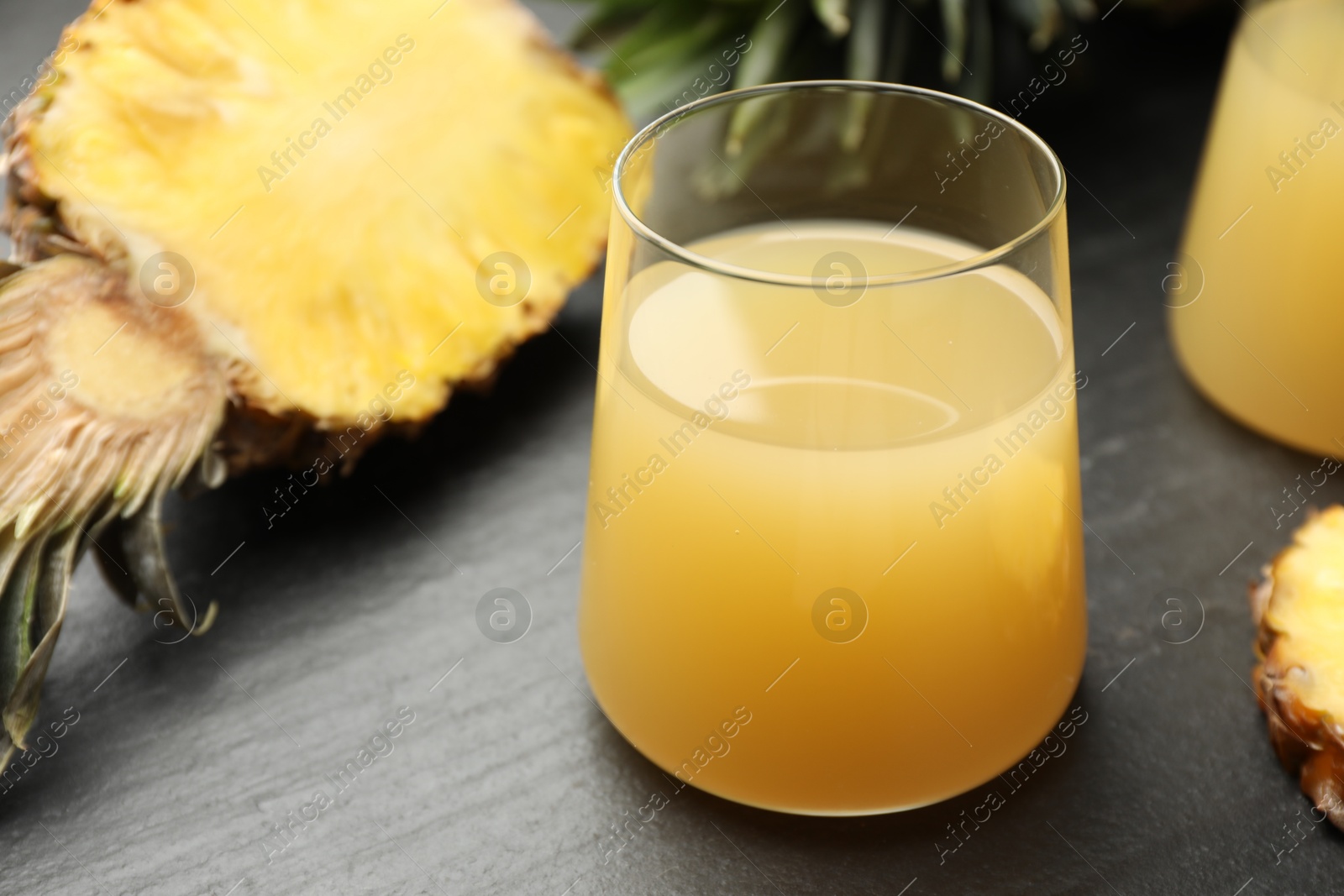 Photo of Tasty pineapple juice in glass and fruit on grey textured table, closeup