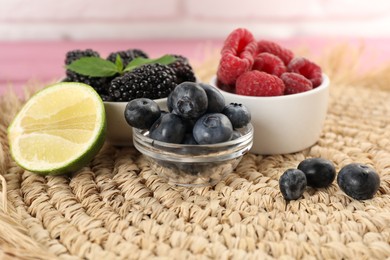 Photo of Delicious berries and lime on wicker mat, closeup