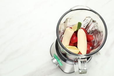 Photo of Blender and fresh ingredients on white marble table, above view. Space for text