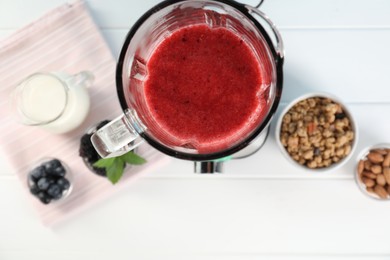 Blender with mixture of ingredients and other fresh products on white wooden table, top view