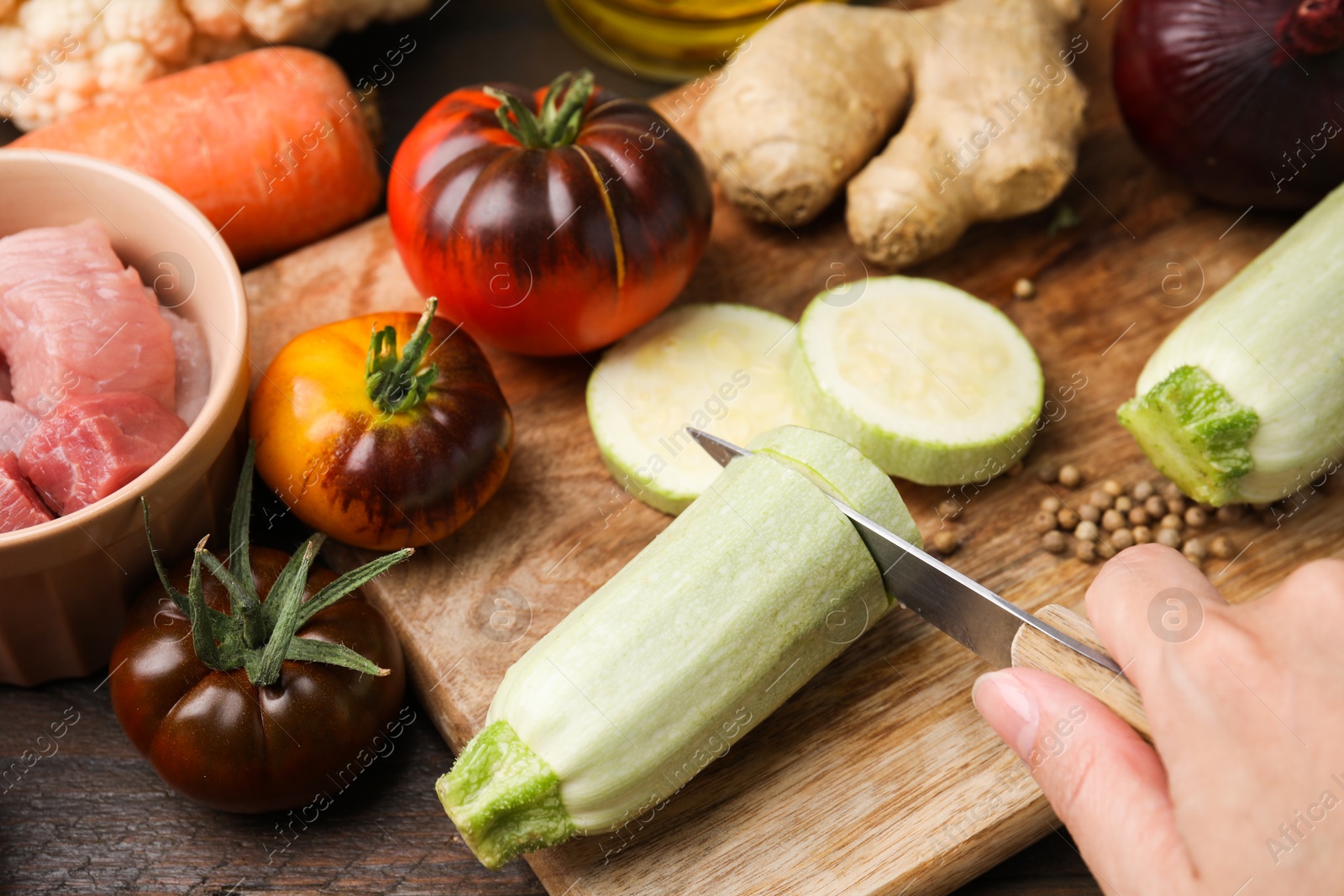 Photo of Cooking tasty stew. Woman cutting zucchini at wooden table, closeup