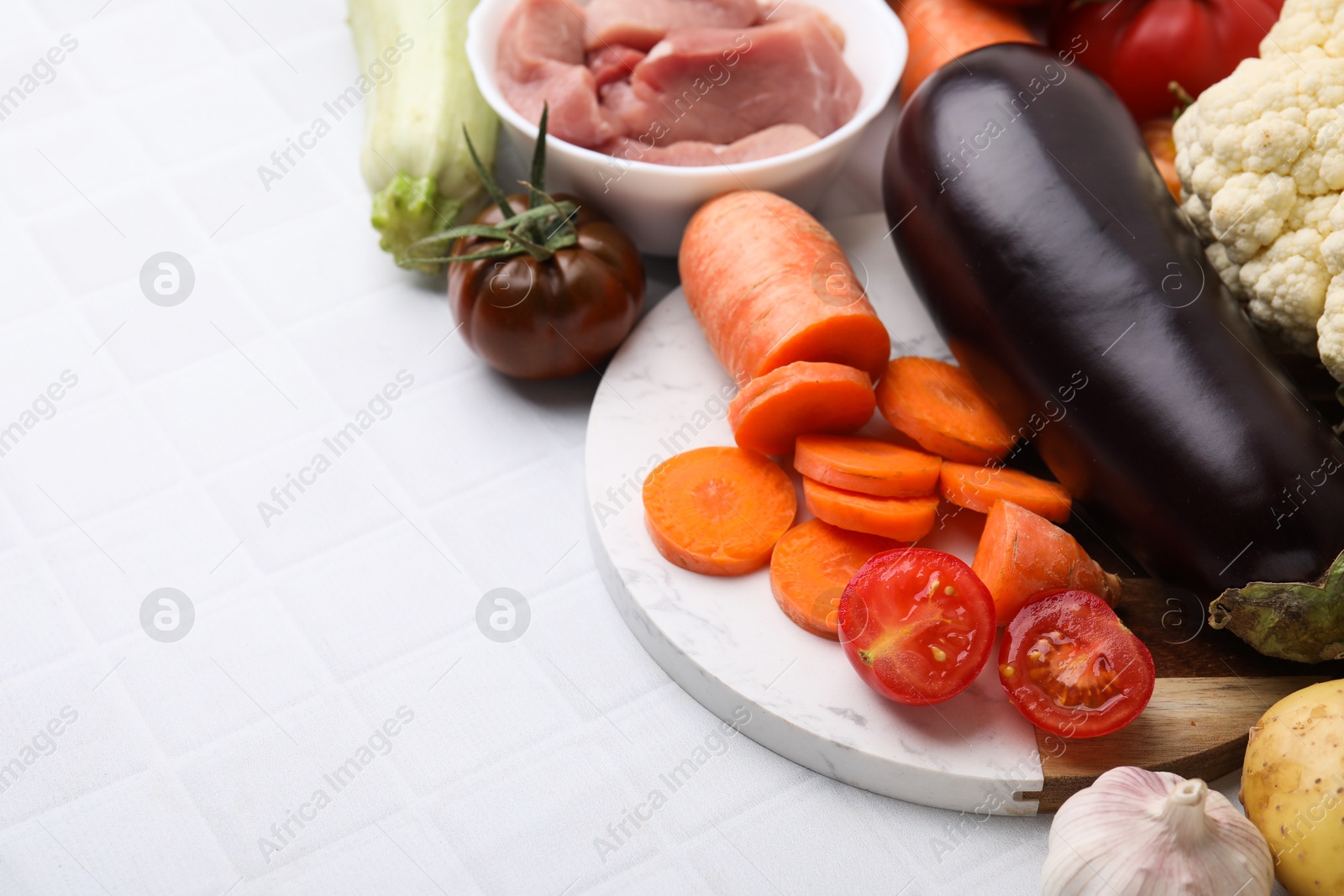 Photo of Different vegetables and raw meat for stew on white tiled table, space for text