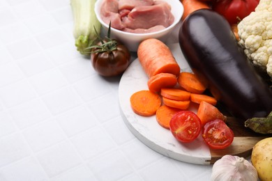 Different vegetables and raw meat for stew on white tiled table, space for text