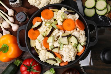 Photo of Cooking stew. Cut raw vegetables in pot on wooden table, flat lay