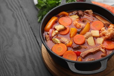 Photo of Tasty homemade stew with vegetables on grey wooden table, closeup. Space for text