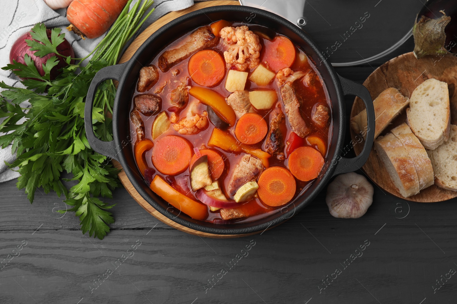 Photo of Tasty homemade stew with vegetables and bread on grey wooden table, flat lay