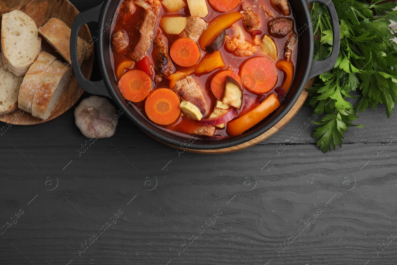 Photo of Tasty homemade stew with vegetables and bread on grey wooden table, flat lay. Space for text