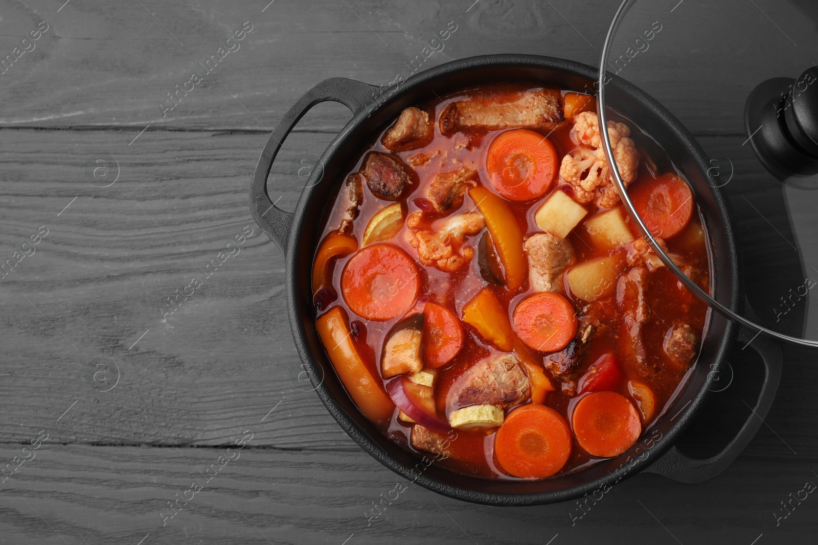 Photo of Tasty homemade stew with vegetables on grey wooden table, top view. Space for text