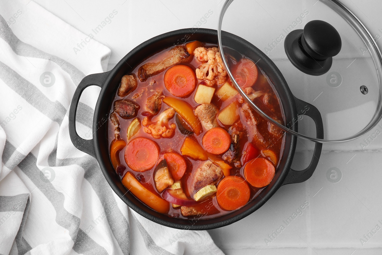 Photo of Tasty homemade stew with vegetables on white tiled table, top view