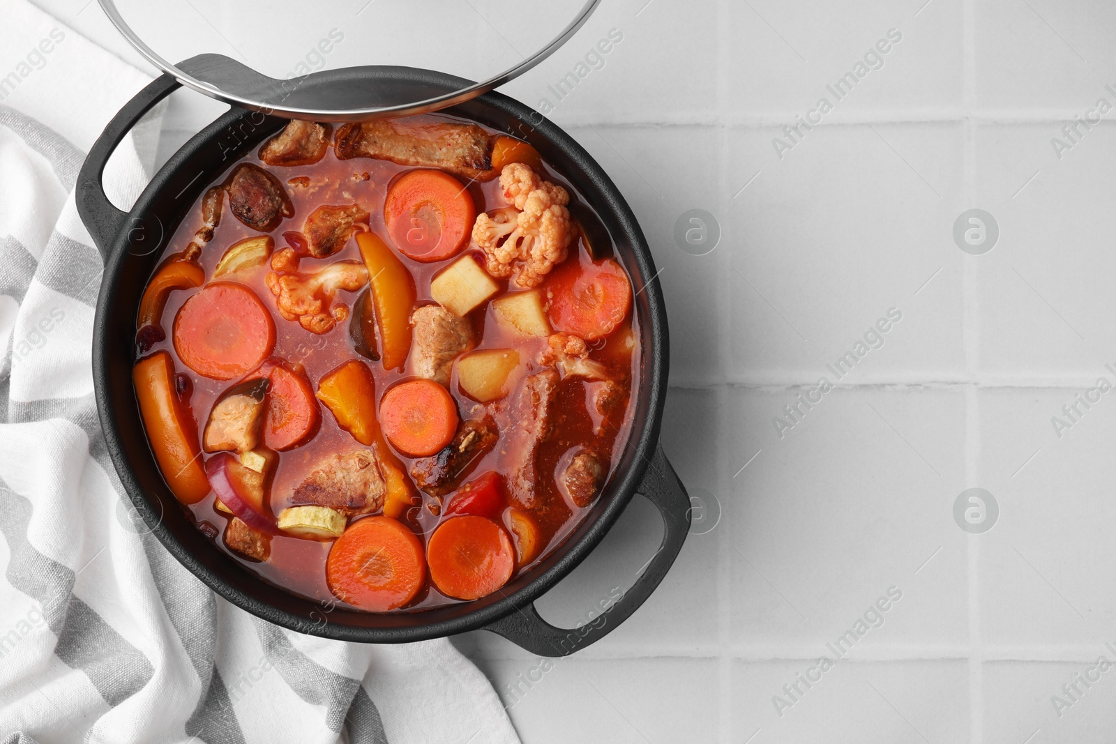 Photo of Tasty homemade stew with vegetables on white tiled table, top view. Space for text