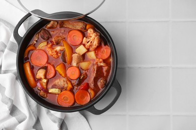 Photo of Tasty homemade stew with vegetables on white tiled table, top view. Space for text