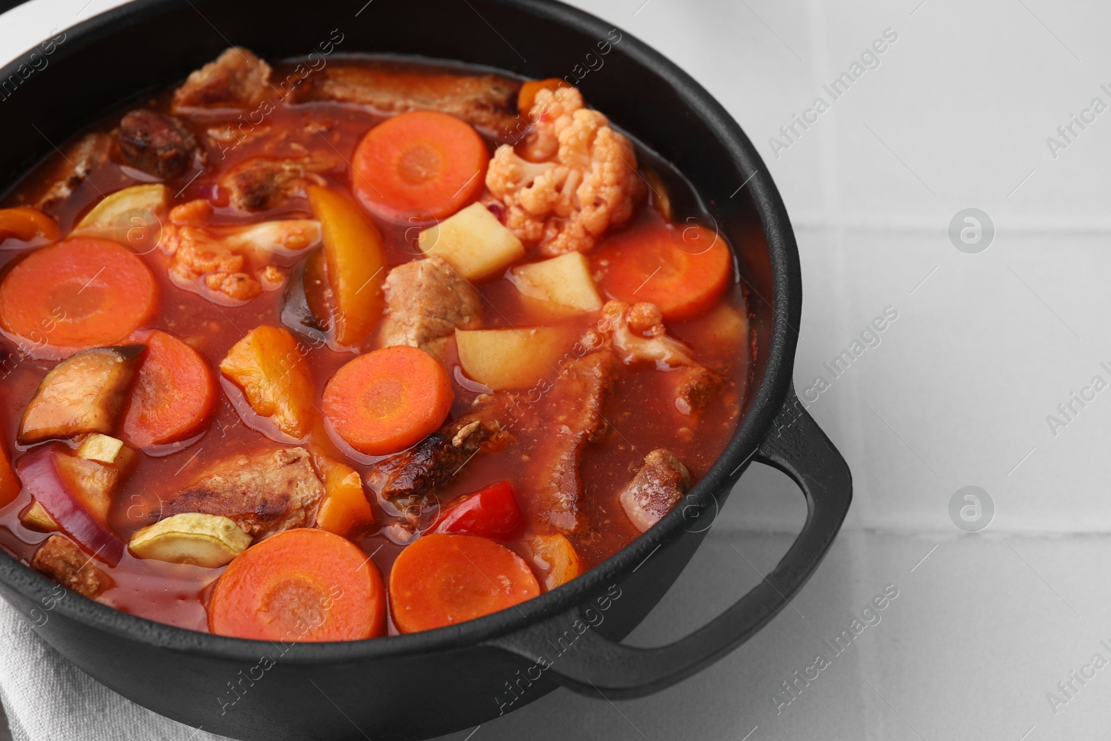 Photo of Tasty homemade stew with vegetables on white tiled table, closeup