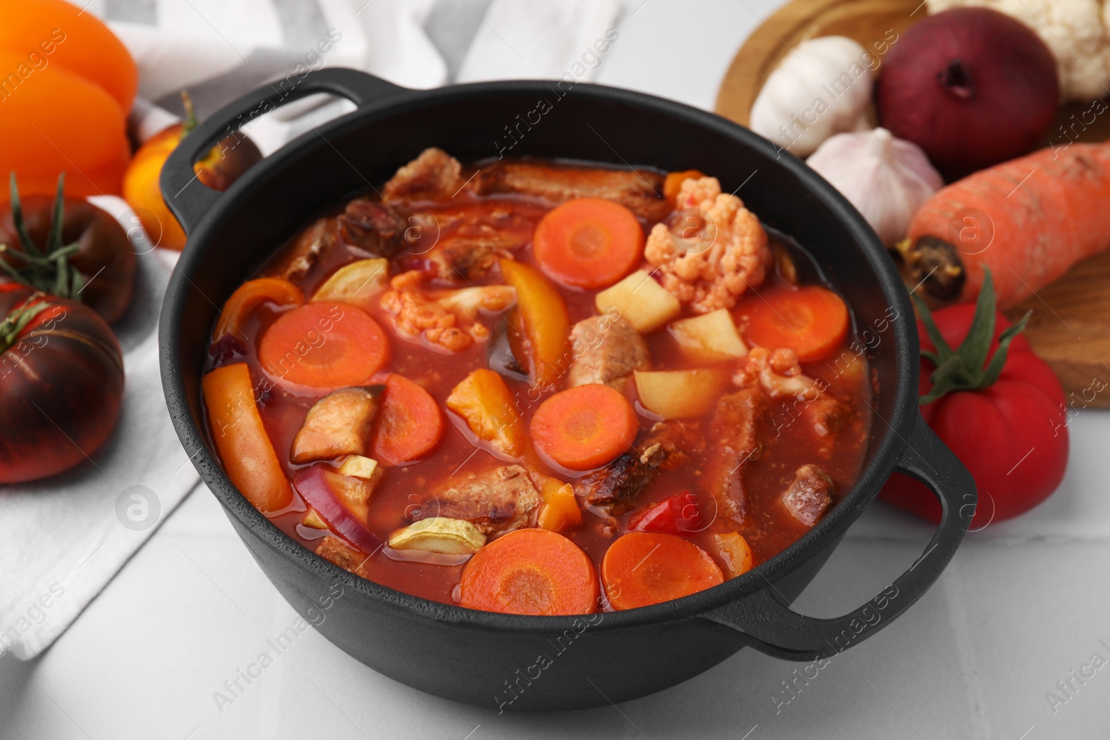 Photo of Tasty homemade stew with vegetables on white tiled table, closeup