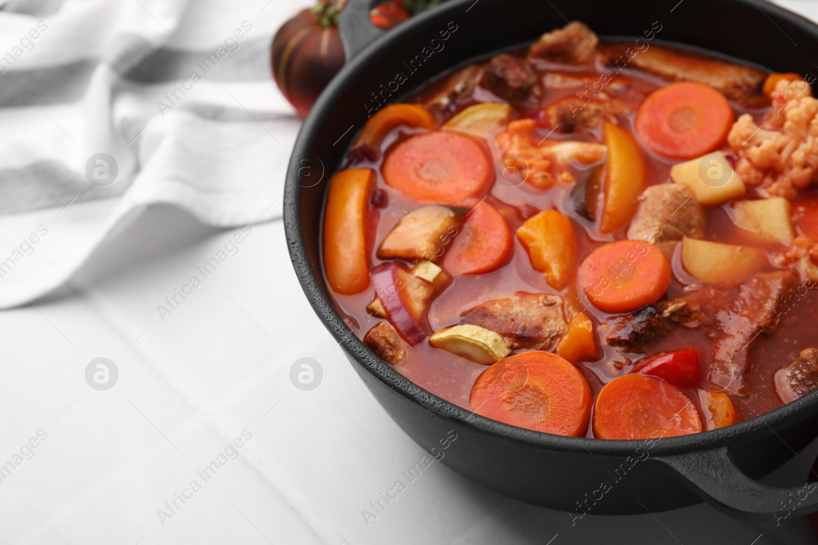 Photo of Tasty homemade stew with vegetables on white tiled table, closeup. Space for text