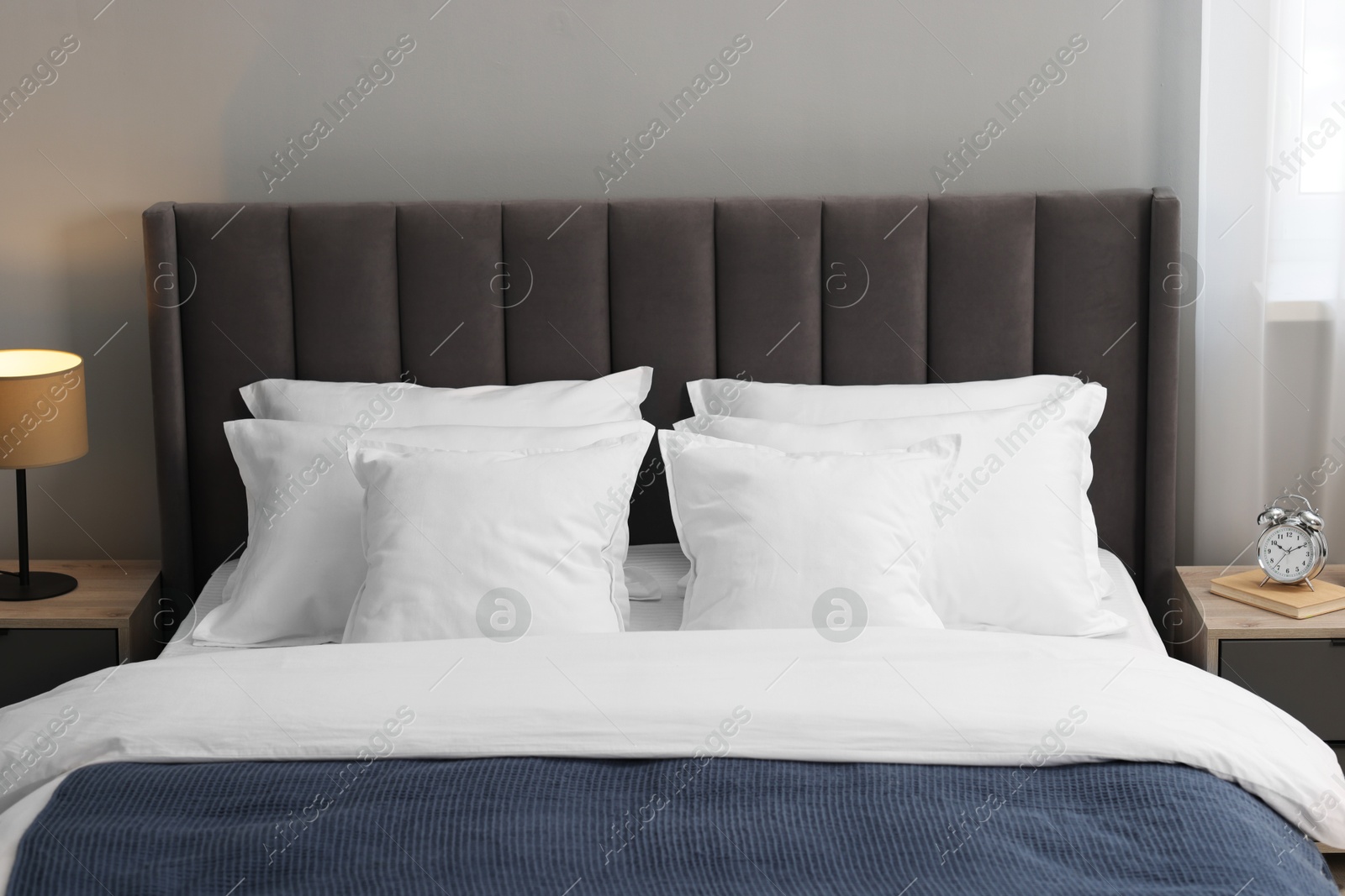 Photo of Many soft pillows on bed and bedside tables at home