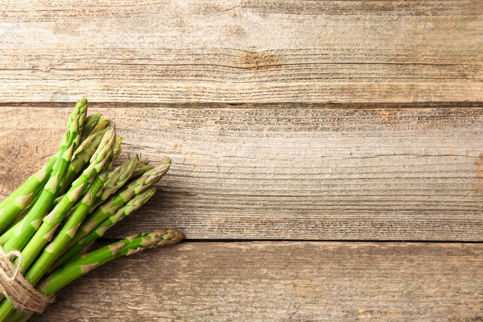 Photo of Bunch of fresh green asparagus stems on wooden table, top view. Space for text