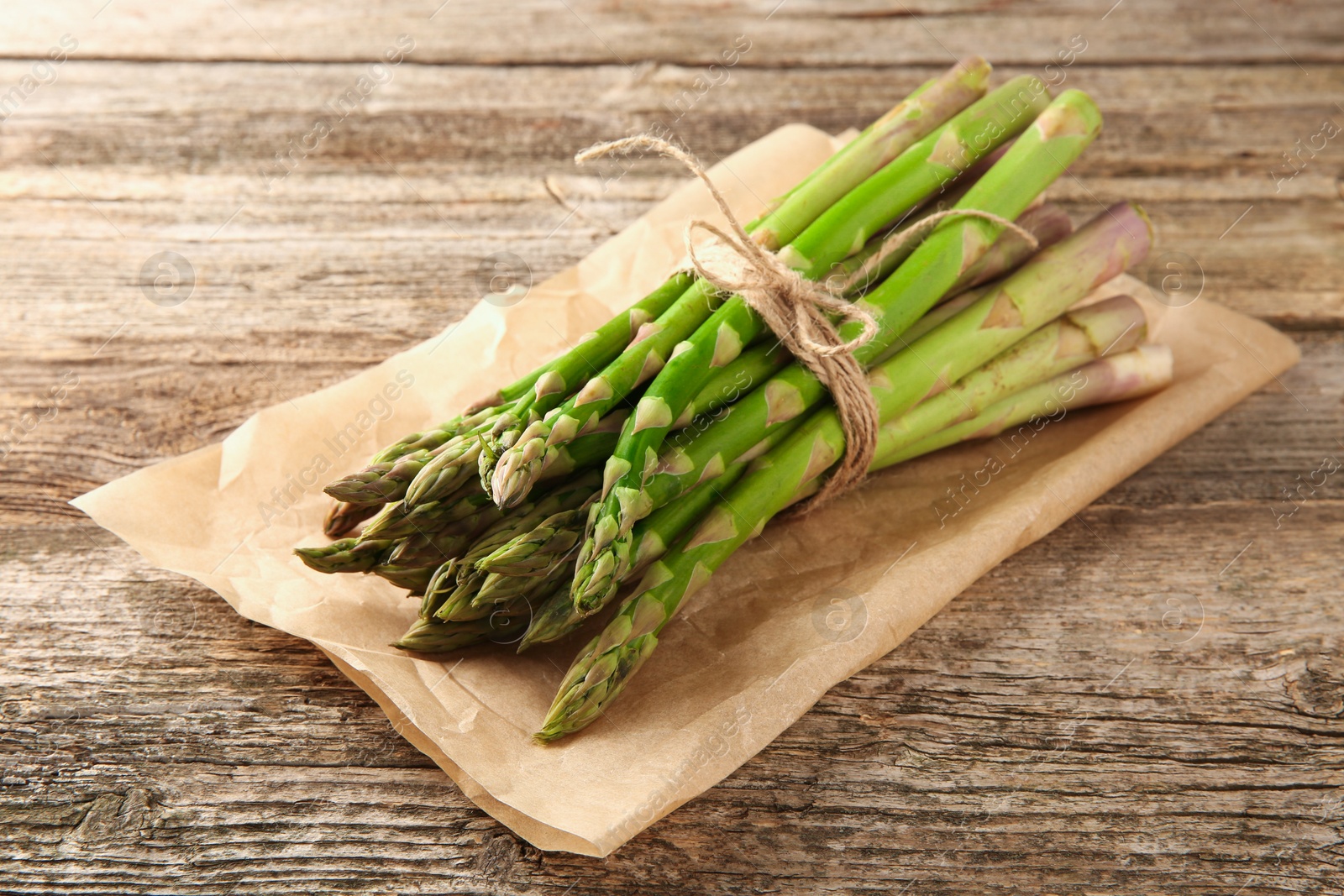 Photo of Bunch of fresh green asparagus stems on wooden table, closeup