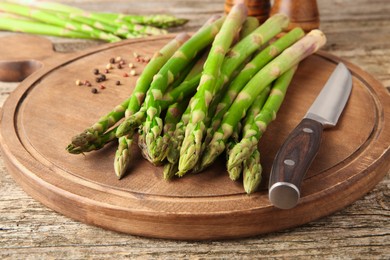 Photo of Board with fresh green asparagus stems, peppercorns and knife on wooden table, closeup