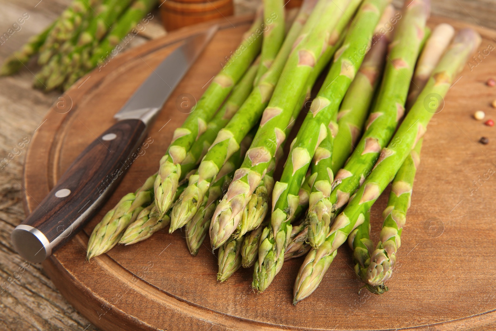 Photo of Board with fresh green asparagus stems and knife on wooden table, closeup