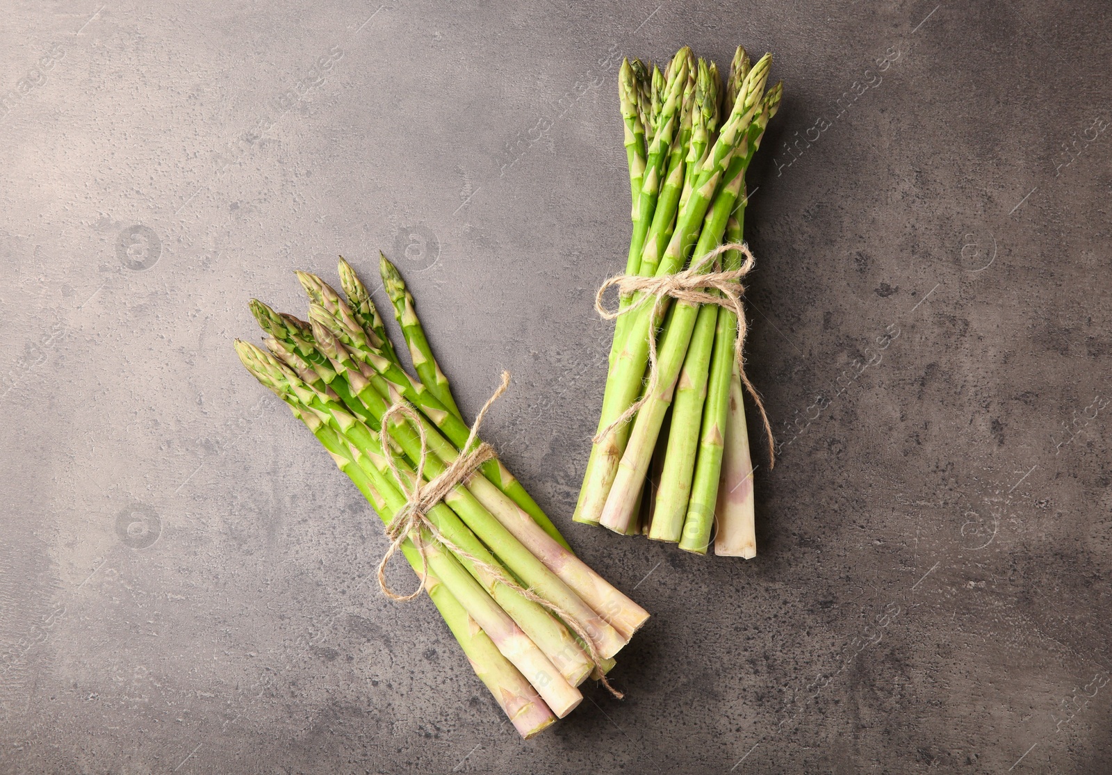 Photo of Bunches of fresh green asparagus stems on grey textured table, flat lay