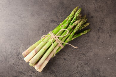 Photo of Bunch of fresh green asparagus stems on grey textured table, top view