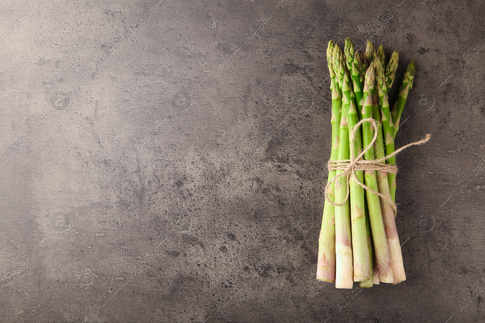 Photo of Bunch of fresh green asparagus stems on grey textured table, top view. Space for text