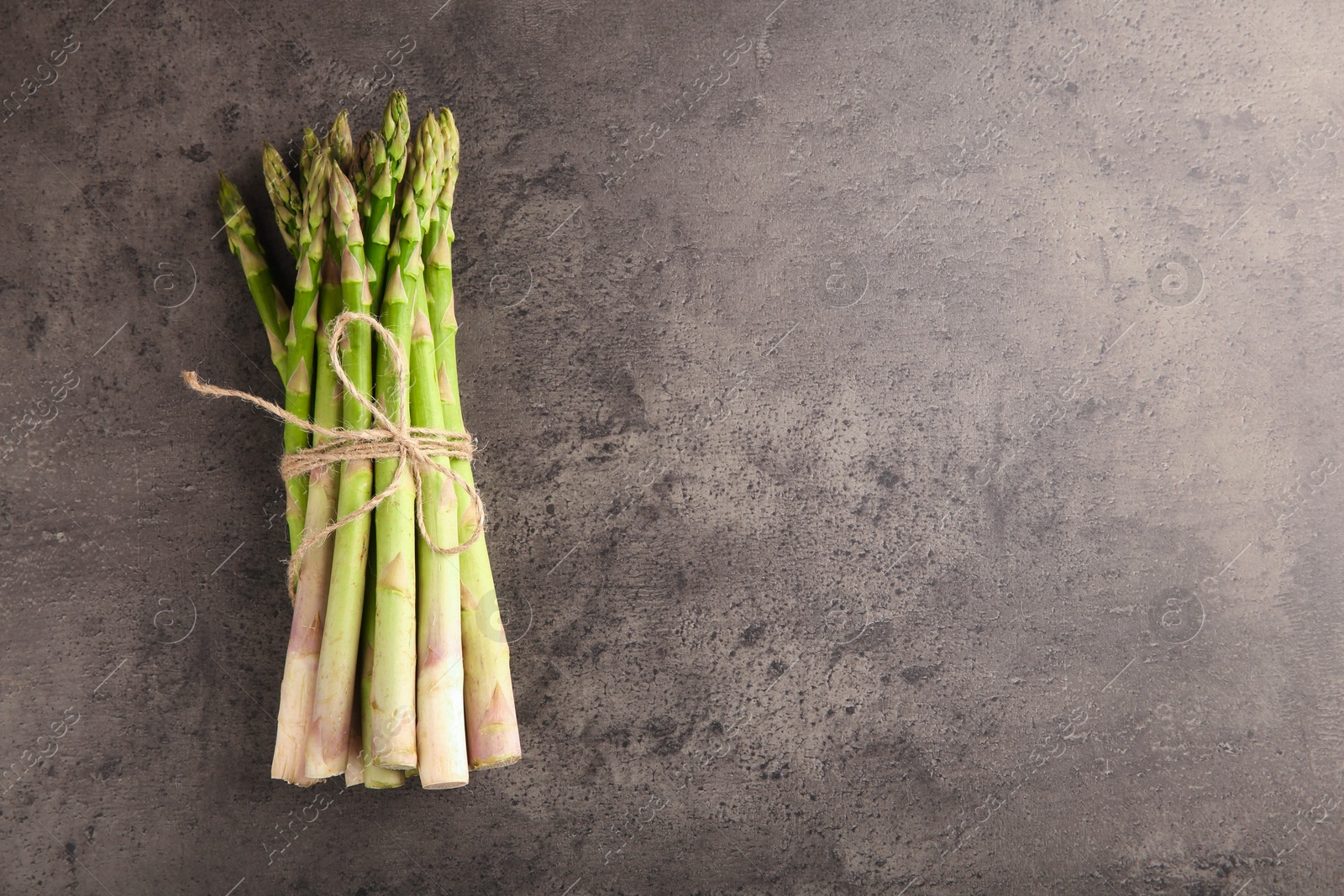 Photo of Bunch of fresh green asparagus stems on grey textured table, top view. Space for text