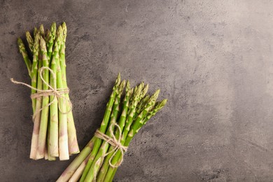 Bunches of fresh green asparagus stems on grey textured table, flat lay. Space for text