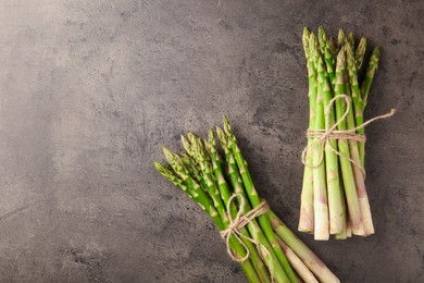 Photo of Bunches of fresh green asparagus stems on grey textured table, flat lay. Space for text