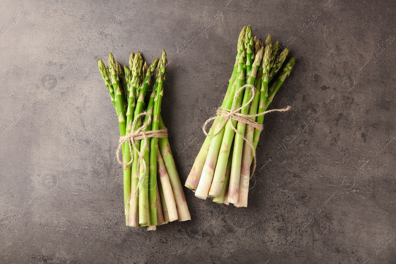 Photo of Bunches of fresh green asparagus stems on grey textured table, flat lay