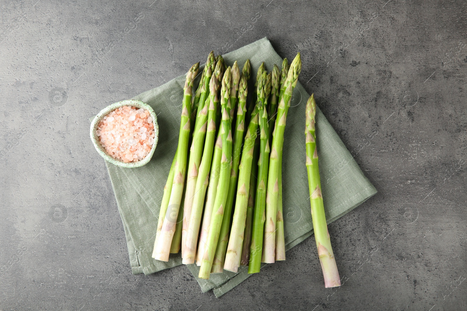 Photo of Fresh green asparagus stems and sea salt on grey textured table, top view