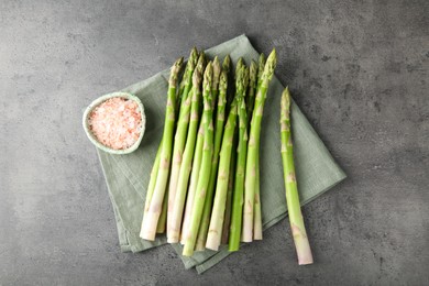 Photo of Fresh green asparagus stems and sea salt on grey textured table, top view