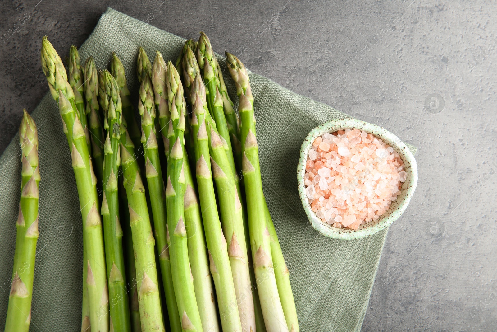 Photo of Fresh green asparagus stems and sea salt on grey textured table, top view