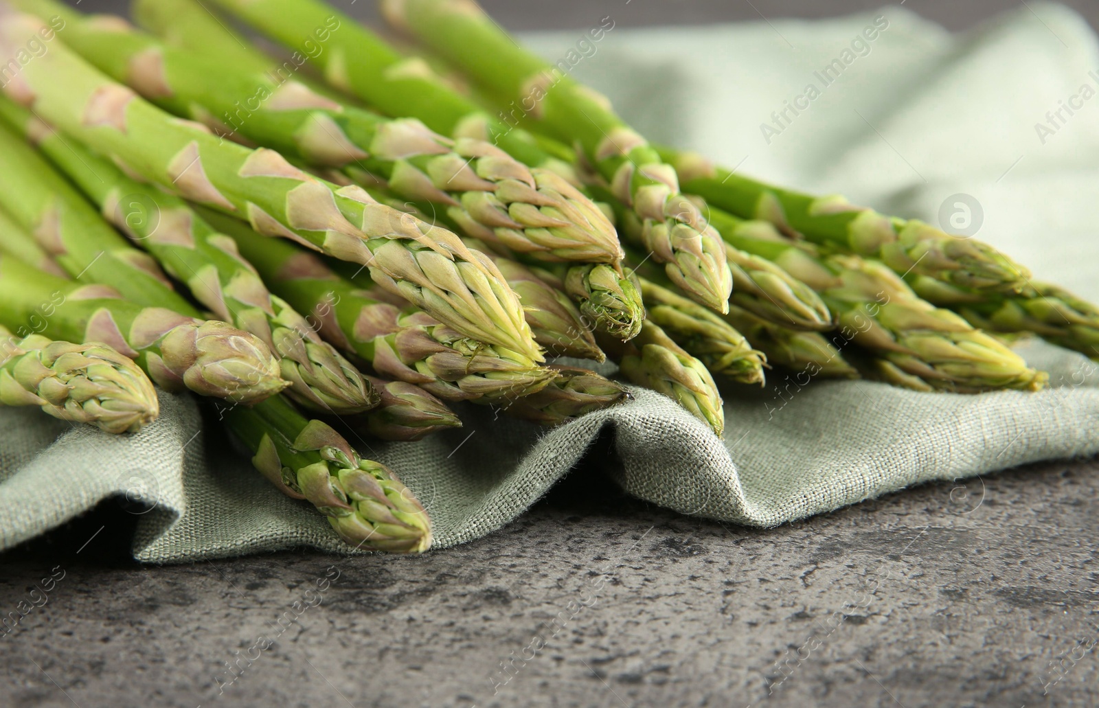 Photo of Fresh green asparagus stems on grey textured table, closeup